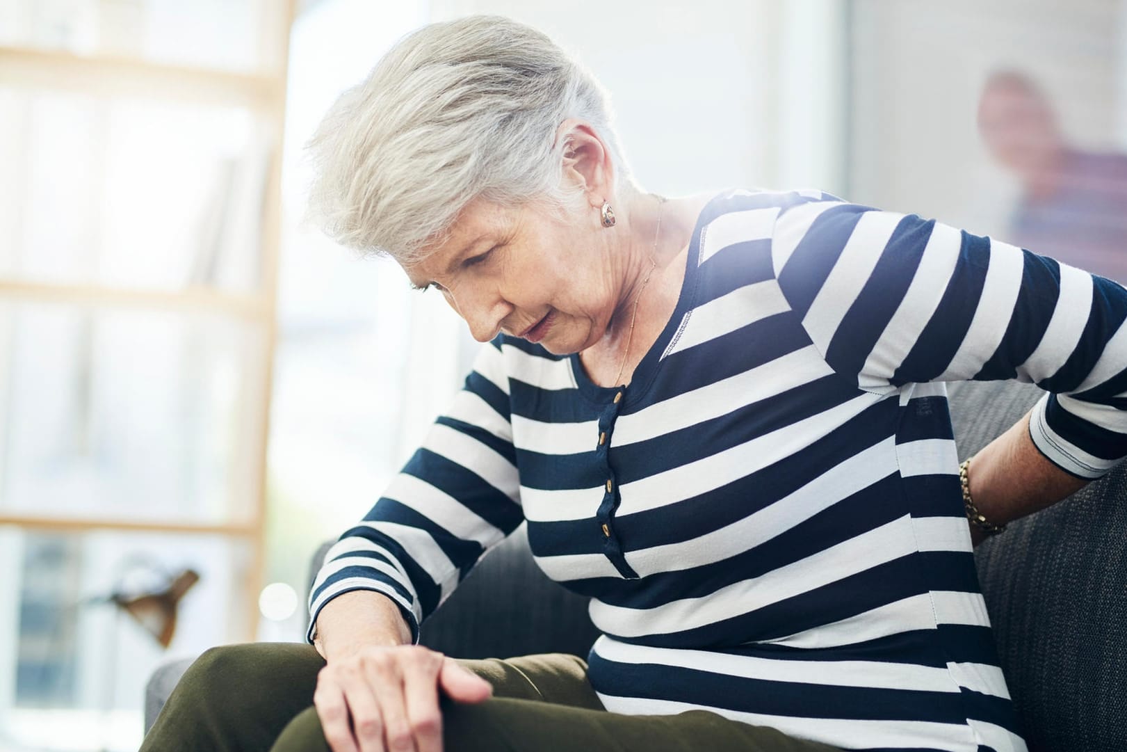 Eine Seniorin greift sich an den Rücken. Nach der Menopause steigt das Risiko für Osteoporose. Die Knochenerkrankung ist oft von starken Rückenschmerzen begleitet.