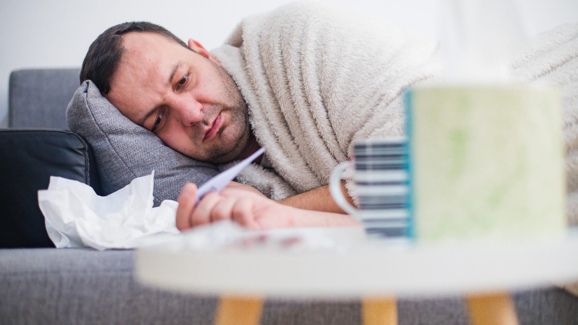 Ein kranker Mann auf dem Sofa: Personen, die an Masern erkrankt sind, sollten sich schonen.