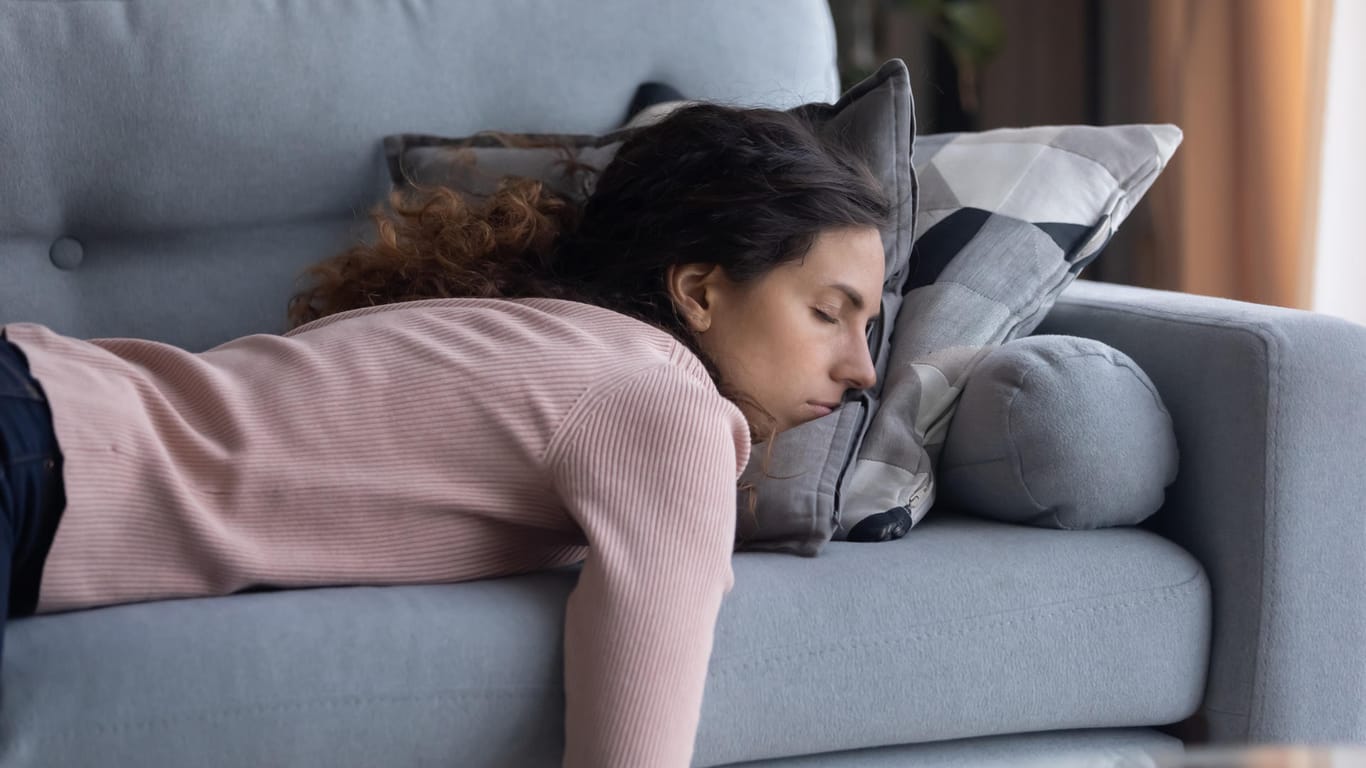 Eine junge Frau liegt erschöpft auf dem Sofa. Chronische Müdigkeit kann von Dauerstress kommen und ist ein Warnsignal des Körpers.