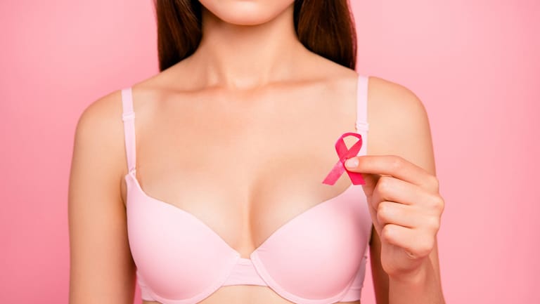 Frau in rosa BH hält rosa Schleife: Die rosa Schleife soll auf das Thema Brustkrebs aufmerksam machen, um Vorsorge, Ursachenforschung und Behandlung zu fördern.