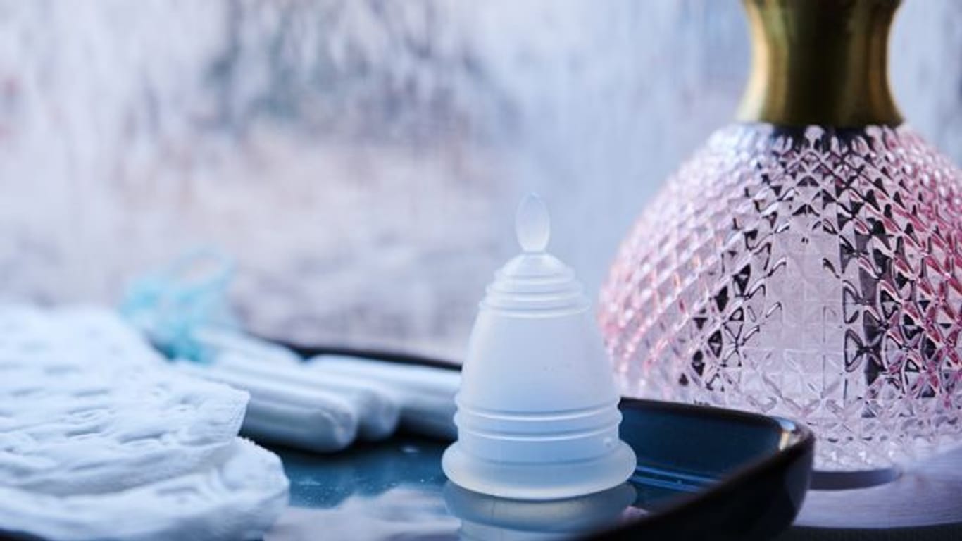 Eine Menstruationstasse, Slipeinlagen und Tampons verschiedener Hersteller liegen in einem Badezimmer.