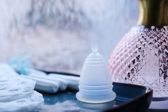 Eine Menstruationstasse, Slipeinlagen und Tampons verschiedener Hersteller liegen in einem Badezimmer.