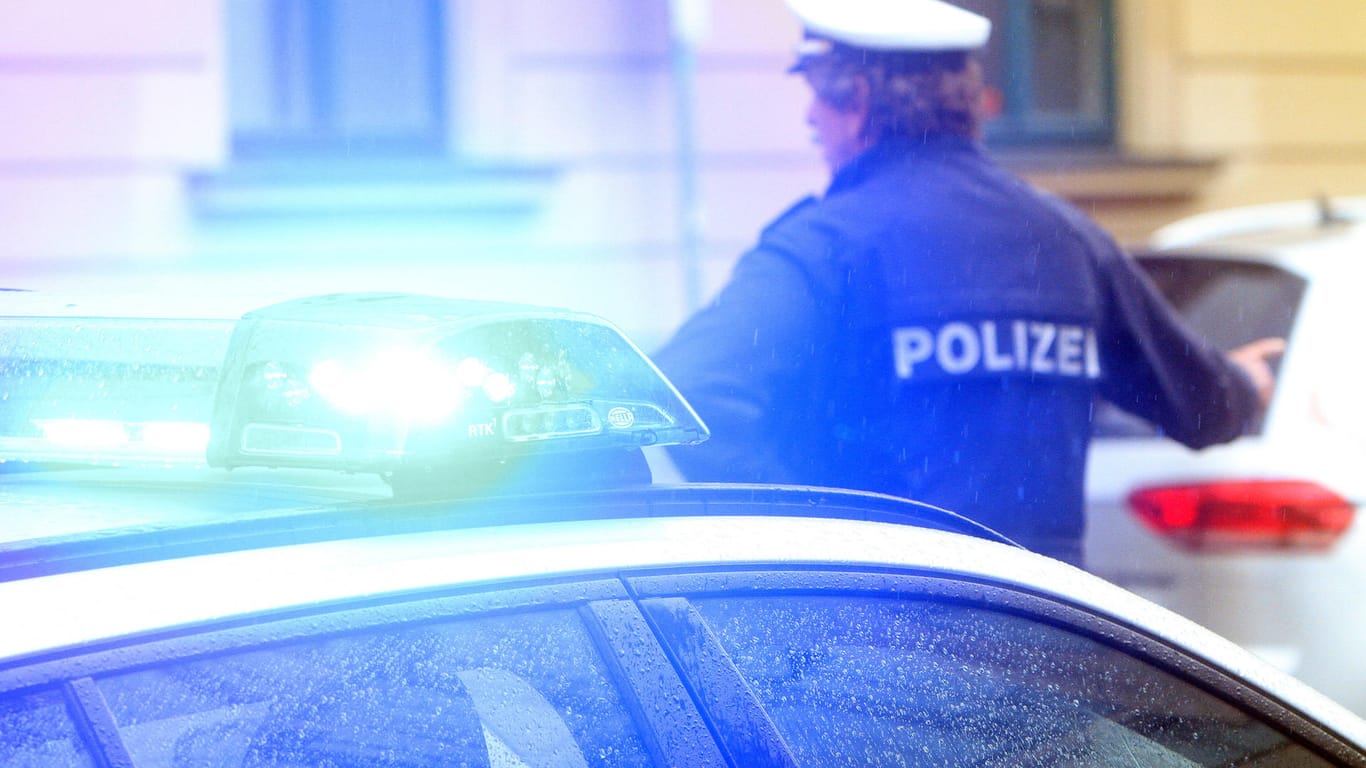 Ein Polizist in Uniform steht vor einem Einsatzwagen der Polizei (Symbolbild). In Hagen mussten Beamte den Bereich des Bahnhofs sperren, weil es einen Verdacht auf eine Bombe gab.