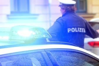 Ein Polizist in Uniform steht vor einem Einsatzwagen der Polizei (Symbolbild). In Hagen mussten Beamte den Bereich des Bahnhofs sperren, weil es einen Verdacht auf eine Bombe gab.
