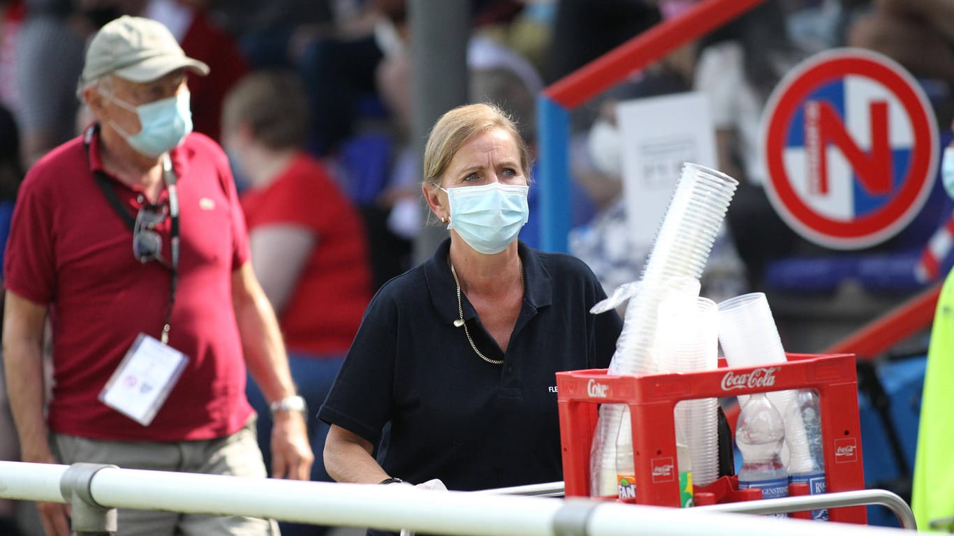 Eine Frau mit Maske fährt einen Verkaufswagen durch ein Fußballstadion (Archivbild). Die Infektionszahlen in Deutschland sinken weiterhin.
