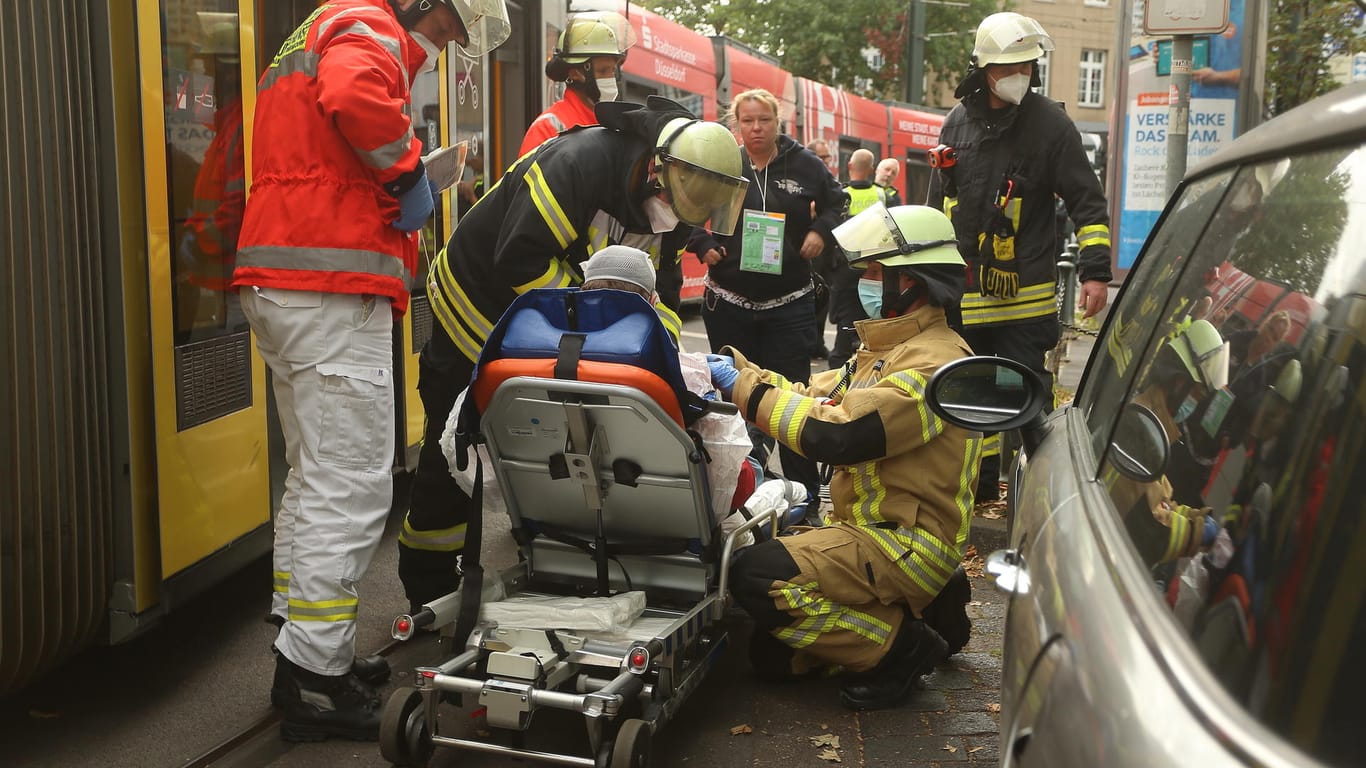 Mitglieder der Feuerwehr versorgen eine verletzte Person, nachdem zwei Straßenbahnen der Düsseldorfer Rheinbahn zusammengestoßen sind.