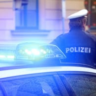 Ein Polizist steht vor einem Einsatzwagen (Symbolbild): In Hannover ist ein 19-Jähriger mit einem spitzen Gegenstand verletzt worden.