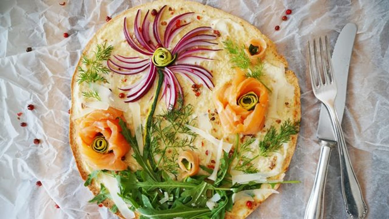 Kreativer Pizza-Belag: Mit roten Zwiebelstreifen, Rucola und Dill sowie Lachs- und Zucchini-Röschen entsteht im Handumdrehen eine Blumenwiese zum Essen.