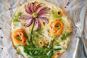 Kreativer Pizza-Belag: Mit roten Zwiebelstreifen, Rucola und Dill sowie Lachs- und Zucchini-Röschen entsteht im Handumdrehen eine Blumenwiese zum Essen.