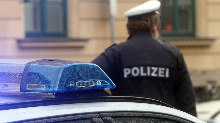 Ein Polizist in Uniform steht vor einem Einsatzwagen der Polizei (Archivbild): In Fellbach bei Stuttgart haben Jugendliche einen Jungen mit einer Waffe bedroht.