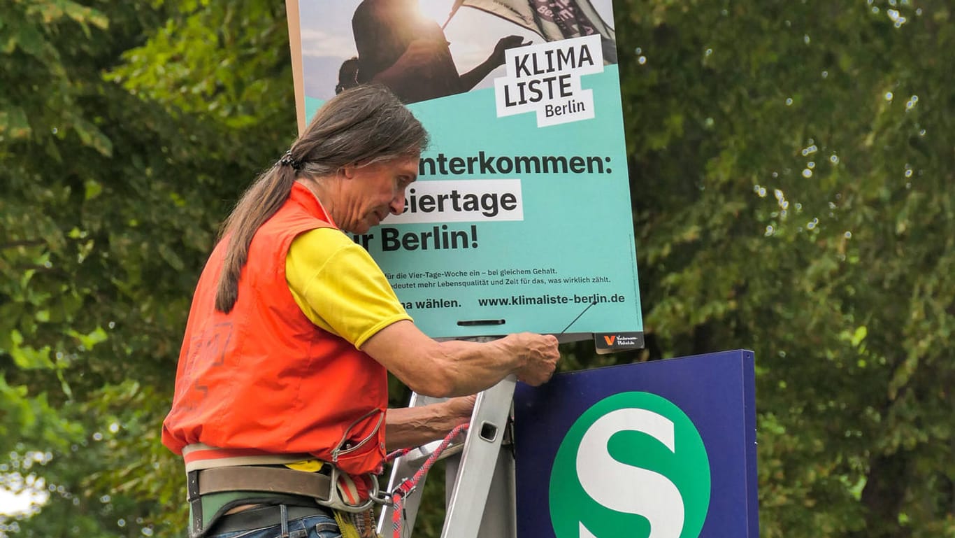 Ein Mitglied der Klimaliste Berlin bringt ein Wahlplakat an: Neben konsequenter Klimapolitik setzt die Kleinpartei auch auf die Idee der Vier-Tage-Woche, um Ressourcen zu schonen.