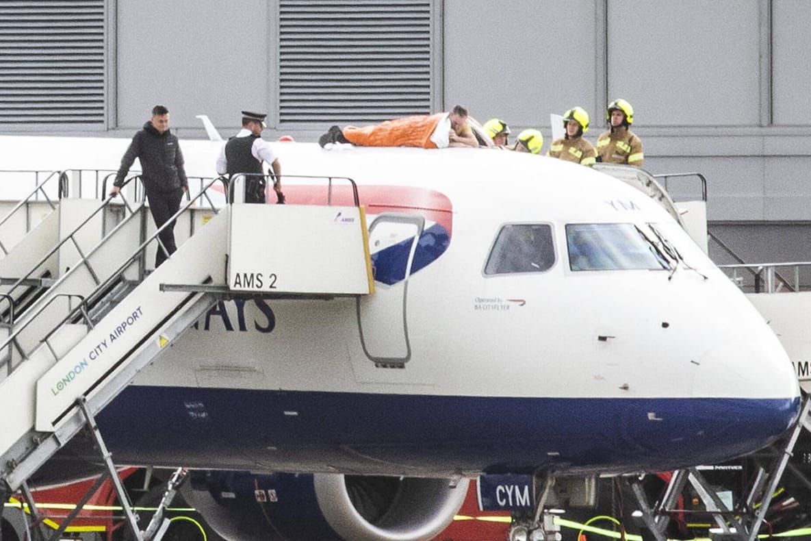 Skurrile Aktion: James Brown (in Orange) kletterte auf eine British-Airways-Maschine und klebte seine Hand an der Flugzeughülle fest.