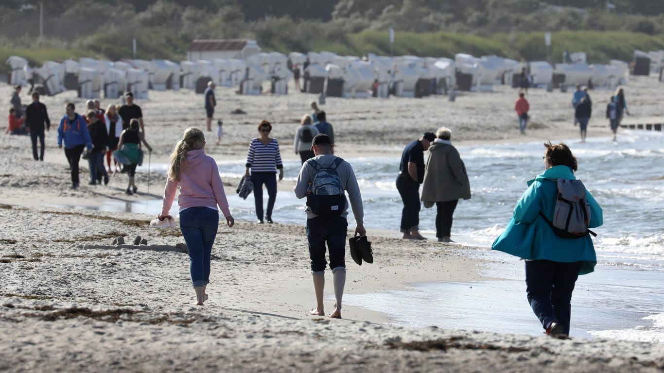 Spaziergänger genießen die Sonne am Strand von Warnemünde: An der Küste kann es auch am Samstag wieder sonnig werden.