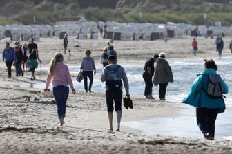 Spaziergänger genießen die Sonne am Strand von Warnemünde: An der Küste kann es auch am Samstag wieder sonnig werden.