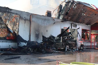 Nach einem Großbrand in einem Supermarkt sind Teile des Daches eingestürzt, ein verbrannter Kleinlaster steht an dem Supermarkt: Das Feuer war am 24.09.2021 morgens in einem Penny-Markt ausgebrochen.