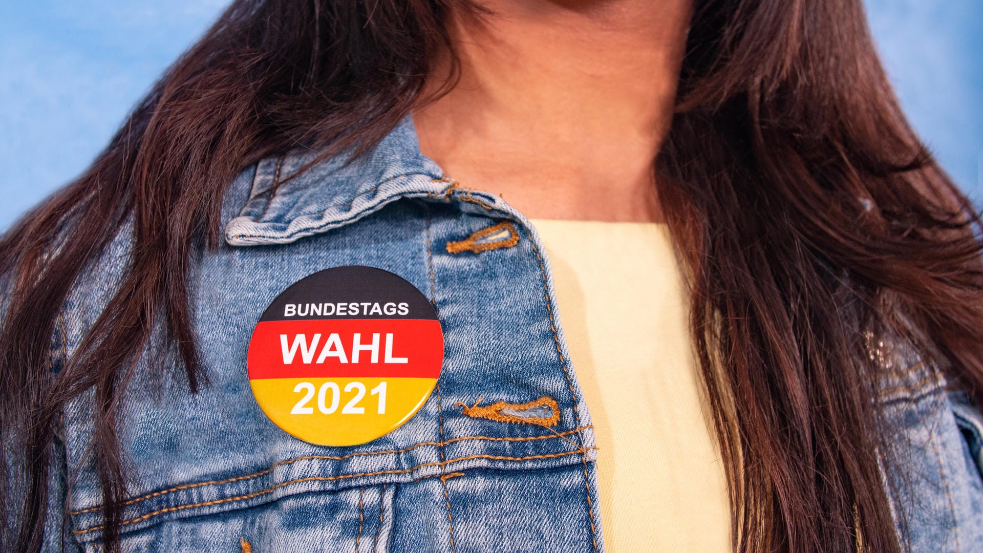 Frau trägt Wah-Button: Verraten Sie uns Ihre Fragen an die Vertreterinnen und Vertreter Ihrer Partei.