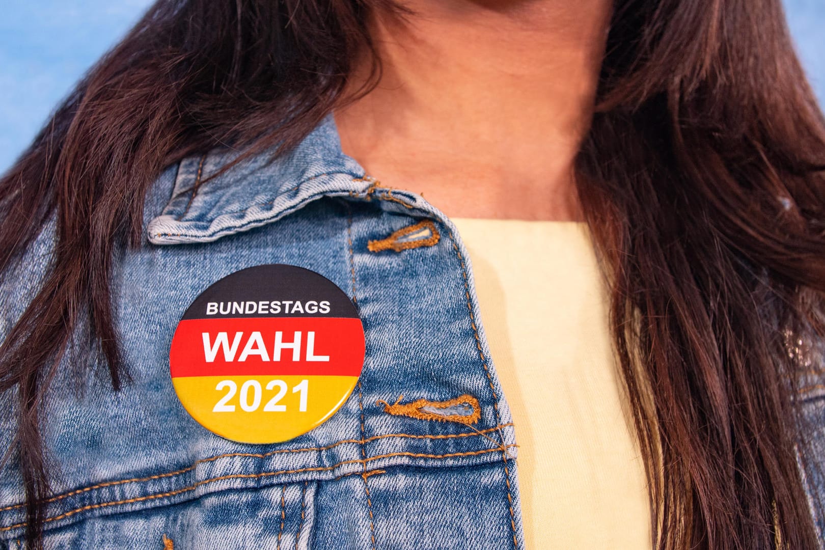 Frau trägt Wah-Button: Verraten Sie uns Ihre Fragen an die Vertreterinnen und Vertreter Ihrer Partei.