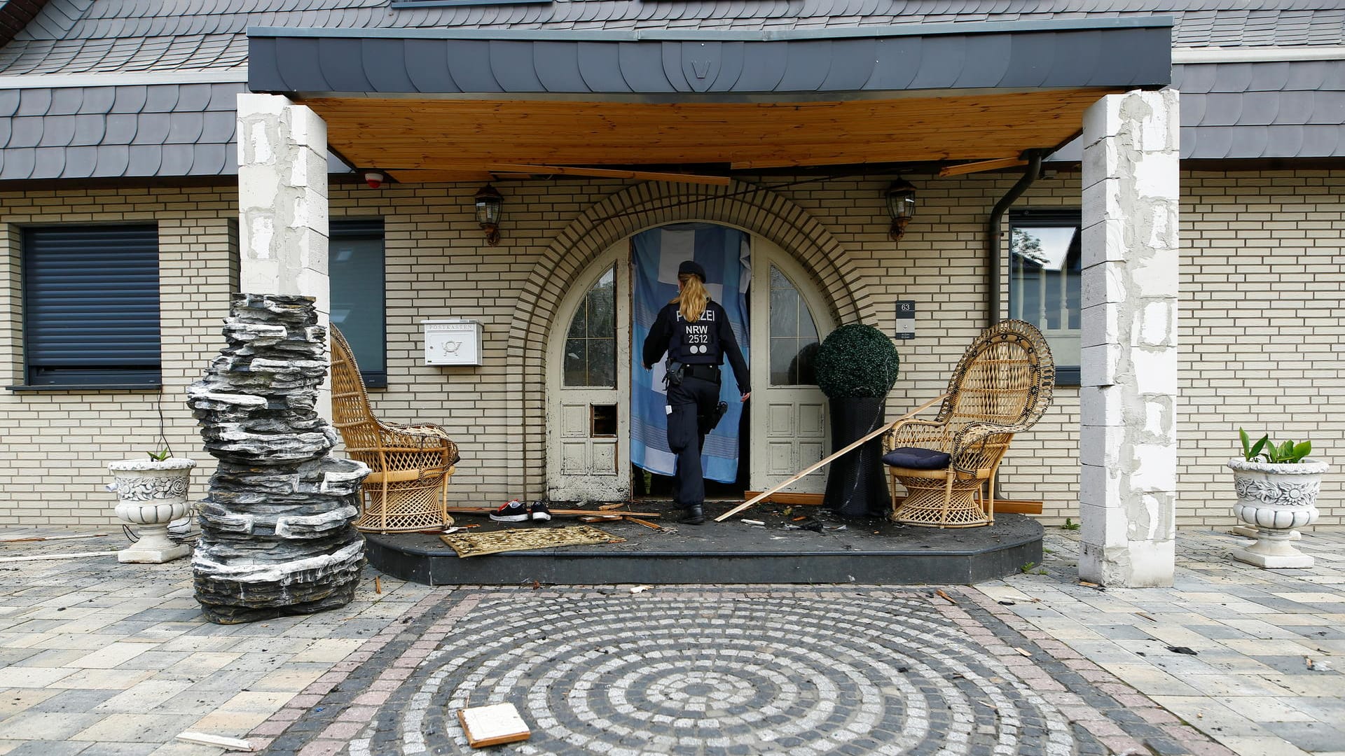 Eine Polizeibeamtin betritt die zerstörte Eingangstür der Villa bei der Razzia im Juni: Die Familie lebt in dem Haus noch immer.