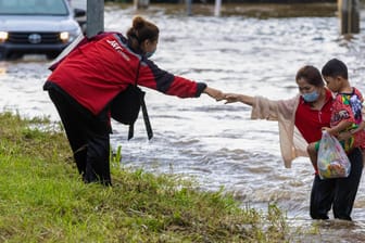 Eine Frau hilft einer anderen mit Kind aus den Fluten: In Thailand haben schwere Regenfälle zu Überschwemmungen geführt.