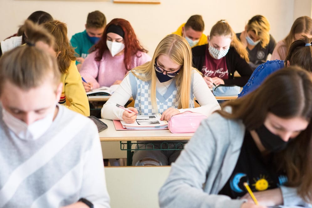 Schülerinnen und Schüler sitzen mit Maske im Unterricht (Archivbild): Die Maskenpflicht am Platz soll in Schulen in Bayern fallen.