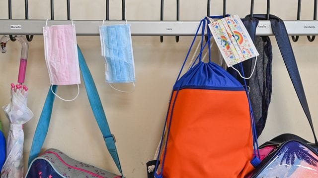 Masken und Taschen hängen in einer Grundschule an Kleiderhaken