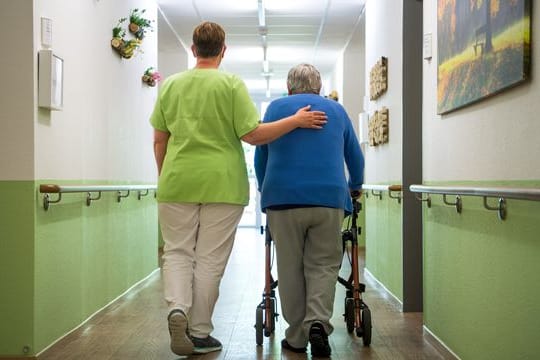 Eine Pflegekraft geht mit einer Bewohnerin eines Seniorenheims