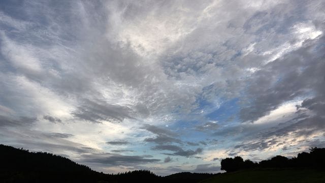 Eine aufgerissene Wolkendecke zieht über ein Wiese hinweg