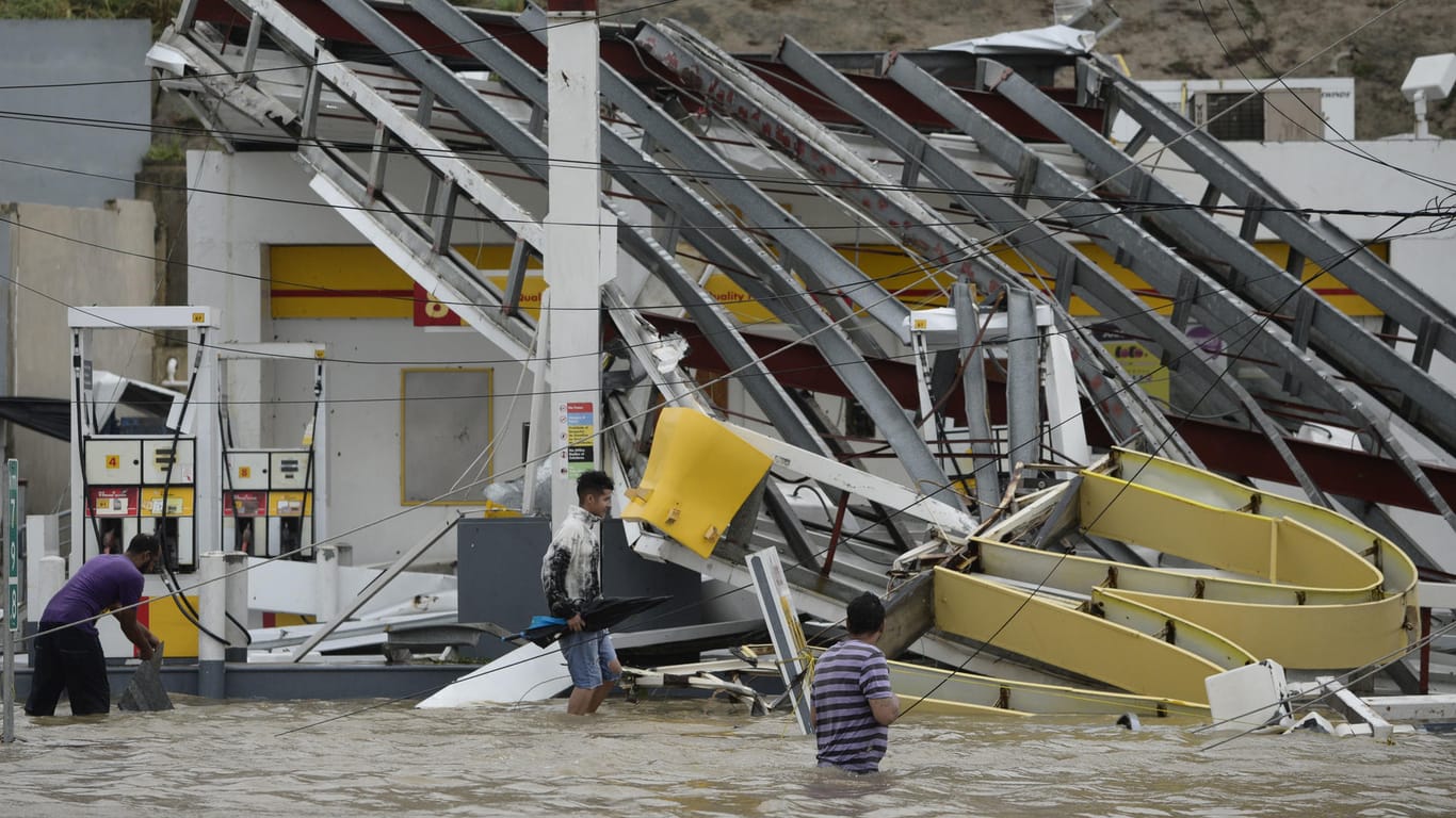 Menschen waten in der Nähe einer durch Hurrikan "Maria" zerstörten Tankstelle durch überflutete Straßen.