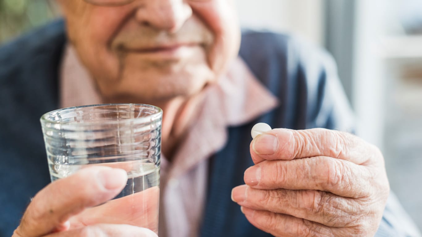 Alter Mann hält ein Glas Wasser und eine Tablette in der Hand.