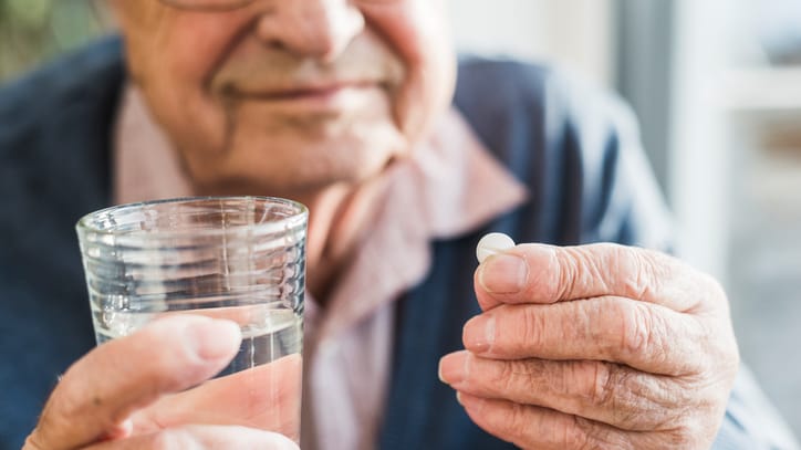 Alter Mann hält ein Glas Wasser und eine Tablette in der Hand.