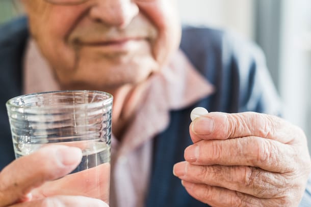 Alter Mann hält ein Glas Wasser und eine Tablette in der Hand.