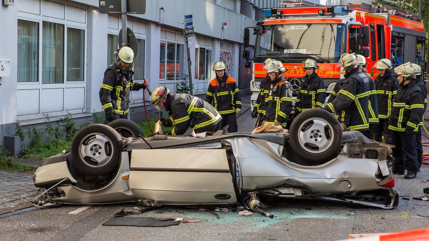 Einsatzkräfte der Feuerwehr arbeiten an einem auf dem Dach liegenden Autowrack: Ein 88 Jahre alter Mann ist mit seinem Auto am Dienstagabend aus dem Parkhaus eines Einkaufscenters in Hamburg 15 Meter in die Tiefe gestürzt.