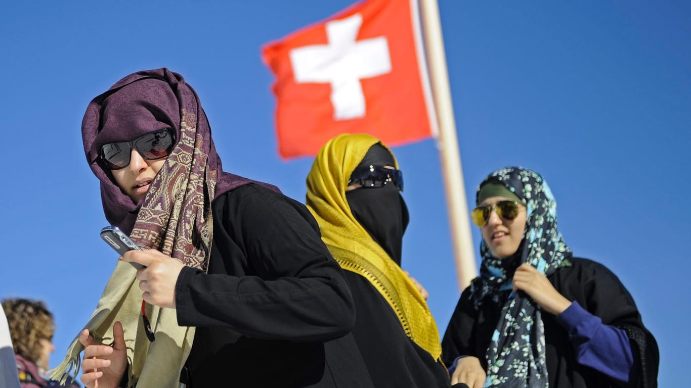 Touristinnen mit Kopftuch vor einer Schweizer Nationalflagge: In der Schweiz führt St. Gallen als zweiter Kanton nach dem Tessin ein Verhüllungsverbot ein.