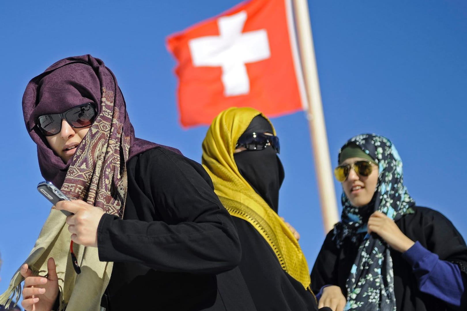 Touristinnen mit Kopftuch vor einer Schweizer Nationalflagge: In der Schweiz führt St. Gallen als zweiter Kanton nach dem Tessin ein Verhüllungsverbot ein.