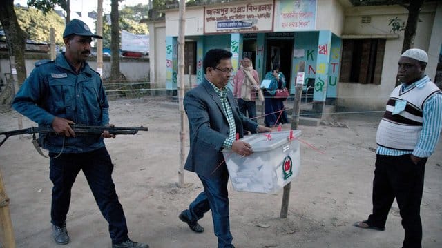 Unter Polizeischutz trägt ein Wahlhelfer nach Ende der Stimmabgabe eine Wahlurne aus einem Wahllokal in Dhaka. Unter Polizeischutz trägt ein Wahlhelfer nach Ende der Stimmabgabe eine Wahlurne aus einem Wahllokal in Dhaka.