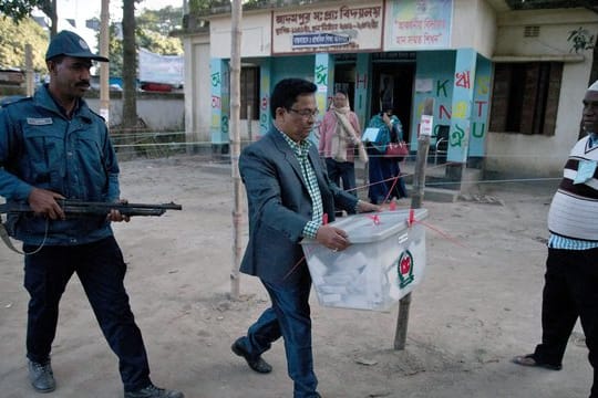 Unter Polizeischutz trägt ein Wahlhelfer nach Ende der Stimmabgabe eine Wahlurne aus einem Wahllokal in Dhaka.