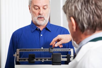 Mann lässt von einem Arzt sein Gewicht bestimmen: Die Häufigkeit der Mahlzeiten ist nicht entscheidend für eine Gewichtszunahme, sondern wie viel und was gegessen wird.