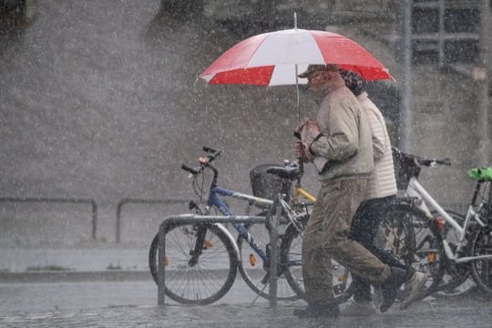 Passanten im Starkregen (Symbolbild): Der DWD warnt in Nürnberg und Umgebung unter anderem vor Gewitter.