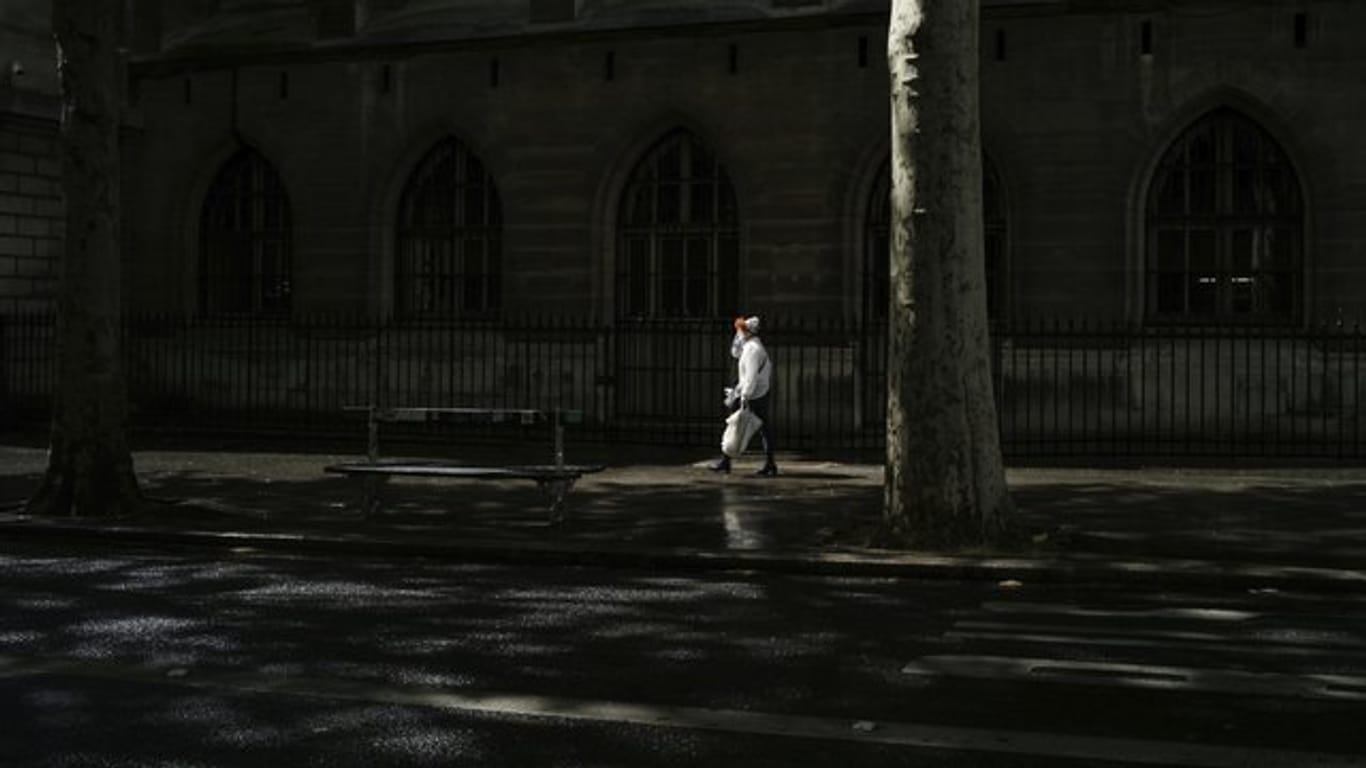 Eine Frau mit Mundschutz geht eine Straße in Paris entlang.