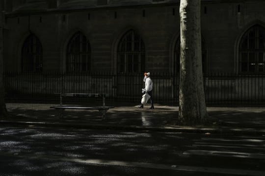 Eine Frau mit Mundschutz geht eine Straße in Paris entlang.