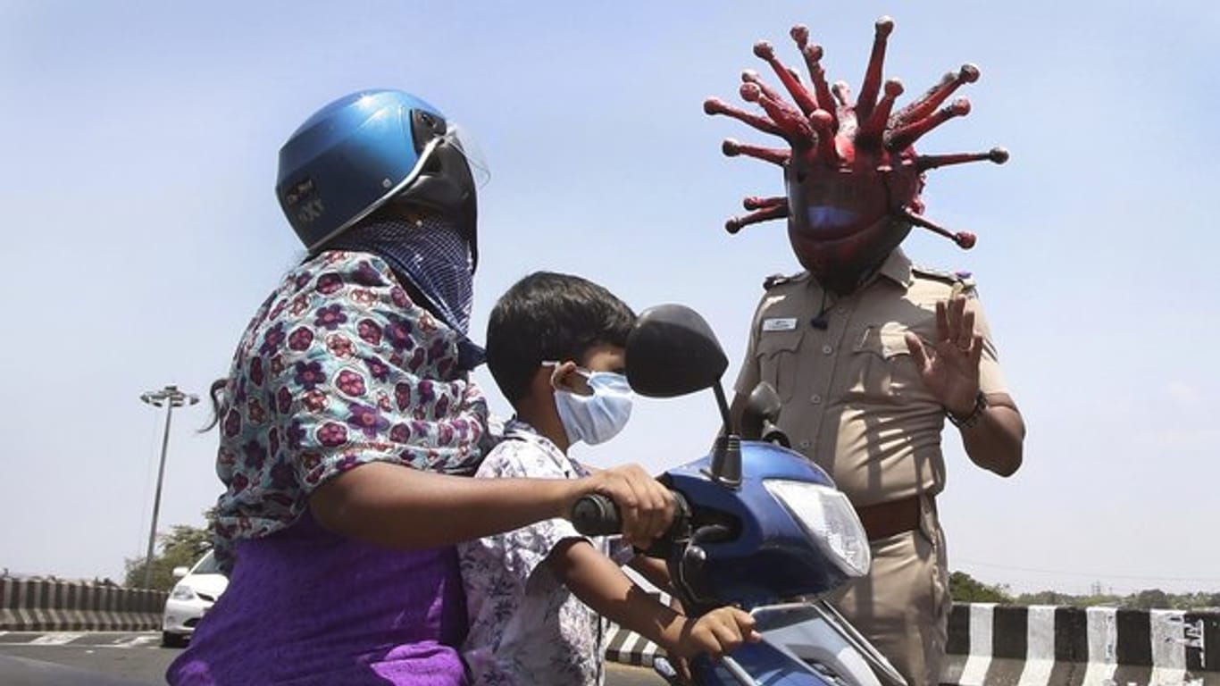 Ein Polizeibeamter im indischen Chennai trägt einen Helm, der einem Virus ähnelt, und weist Pendler auf die Einhaltung der Ausgangsbeschränkungen hin.