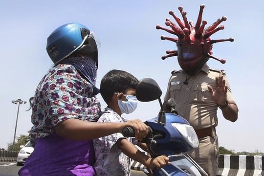 Ein Polizeibeamter im indischen Chennai trägt einen Helm, der einem Virus ähnelt, und weist Pendler auf die Einhaltung der Ausgangsbeschränkungen hin.