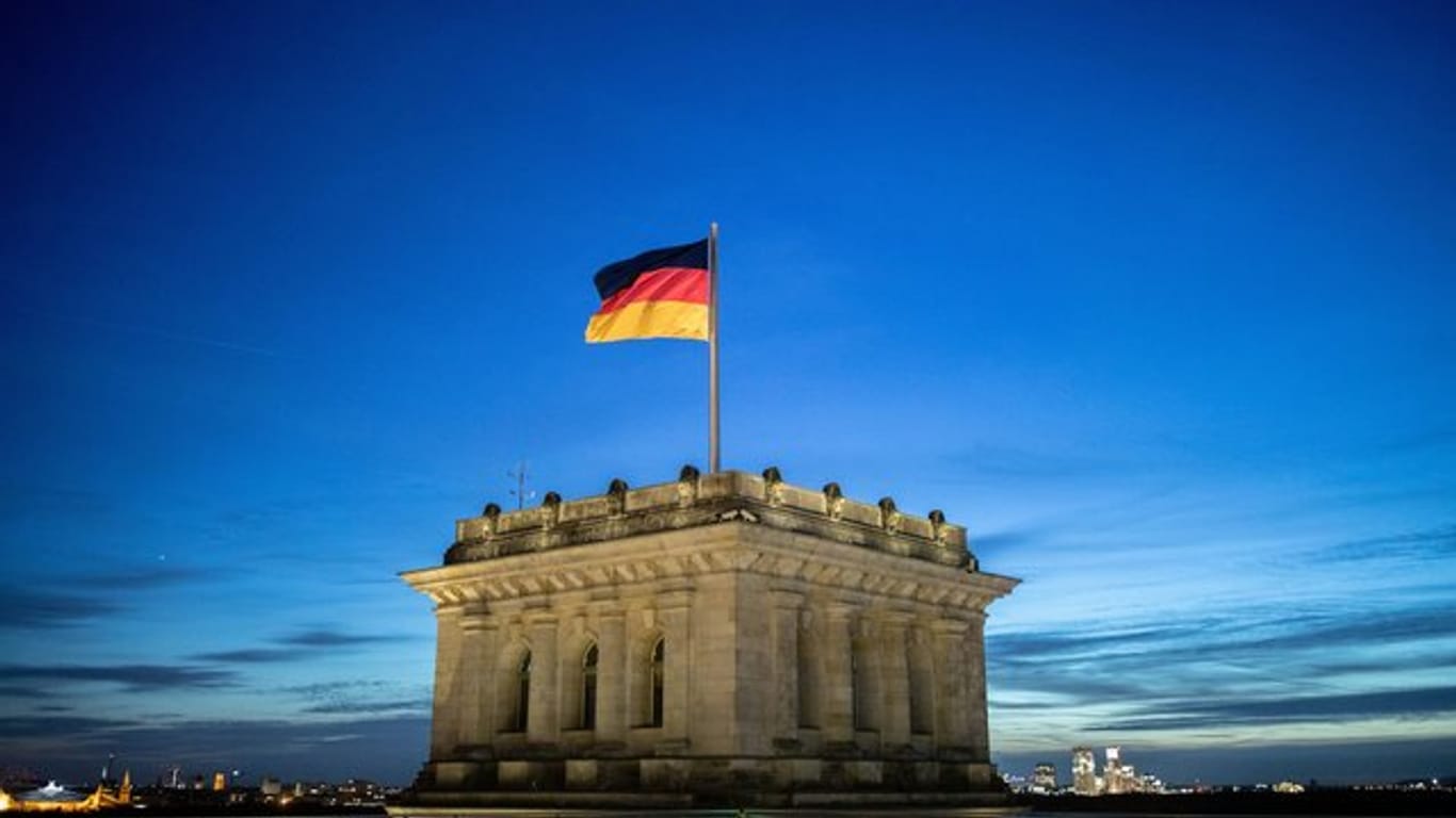 Die Deutschlandfahne weht vor dem Abendhimmel auf dem Reichstagsgebäude im Wind.