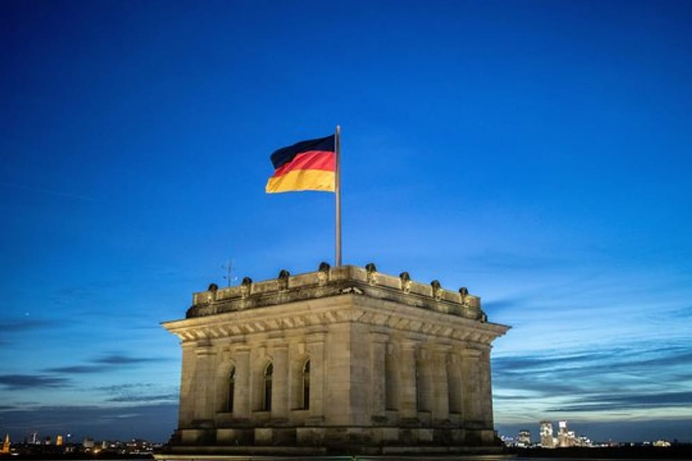 Die Deutschlandfahne weht vor dem Abendhimmel auf dem Reichstagsgebäude im Wind.