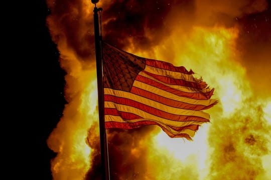 Eine US-Flagge weht vor einem Feuer, das bei Protesten vor dem Gebäude einer Strafvollzugsanstalt in Kenosha lodert.