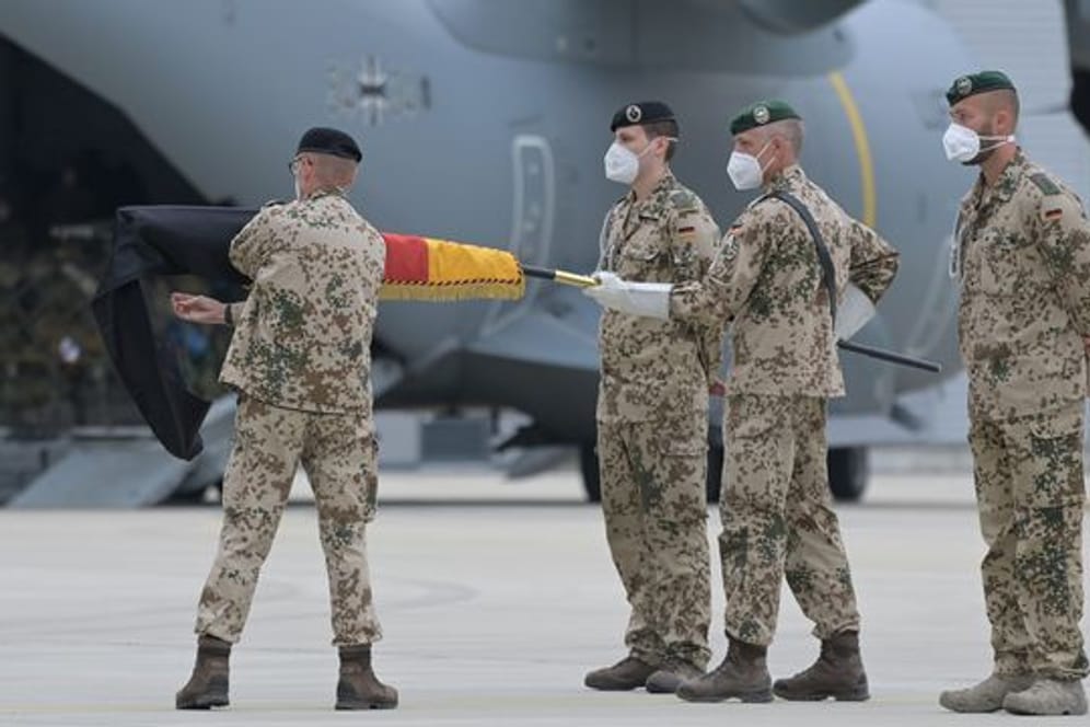 Brigadegeneral Ansgar Meyer (l), der letzte Befehlshaber der Bundeswehr in Afghanistan, rollt vor dem Transportflugzeug vom Typ Airbus A400M der Luftwaffe die Truppenfahne ein.