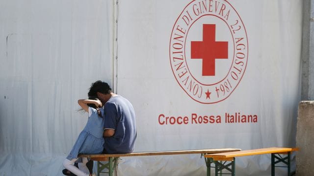 Ein Mann und ein Kind sitzen in einem Einsatzzentrum des italienischen Roten Kreuzes, Croce Rossa Italiana (CRI).