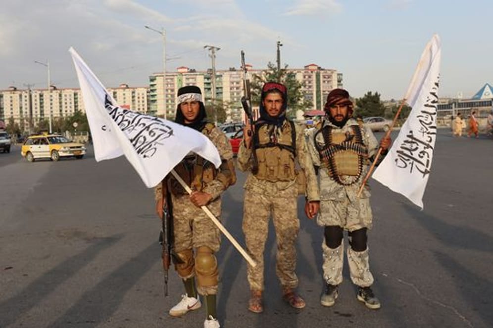 Kämpfer der Taliban stehen mit Flaggen auf einer Straße in der afghanischen Hauptstadt Kabul.