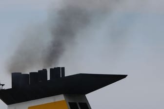Eine dunkle Abgaswolke steigt aus dem Schornstein eines Fährschiffs bei der Ausfahrt aus dem Seehafen.