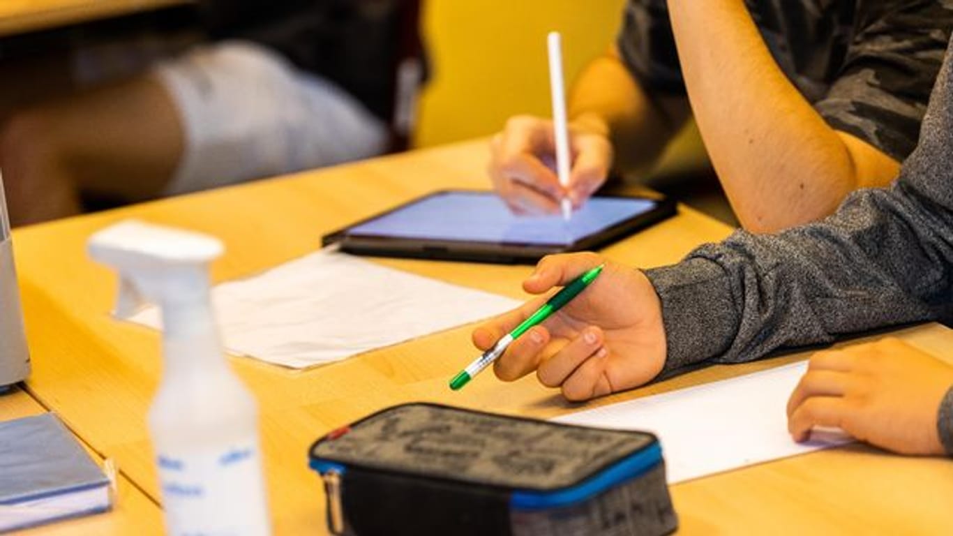 Ein Schüler hält beim Unterricht in seiner Klasse einen Stift, während ein anderer mit einem Tablet arbeitet.